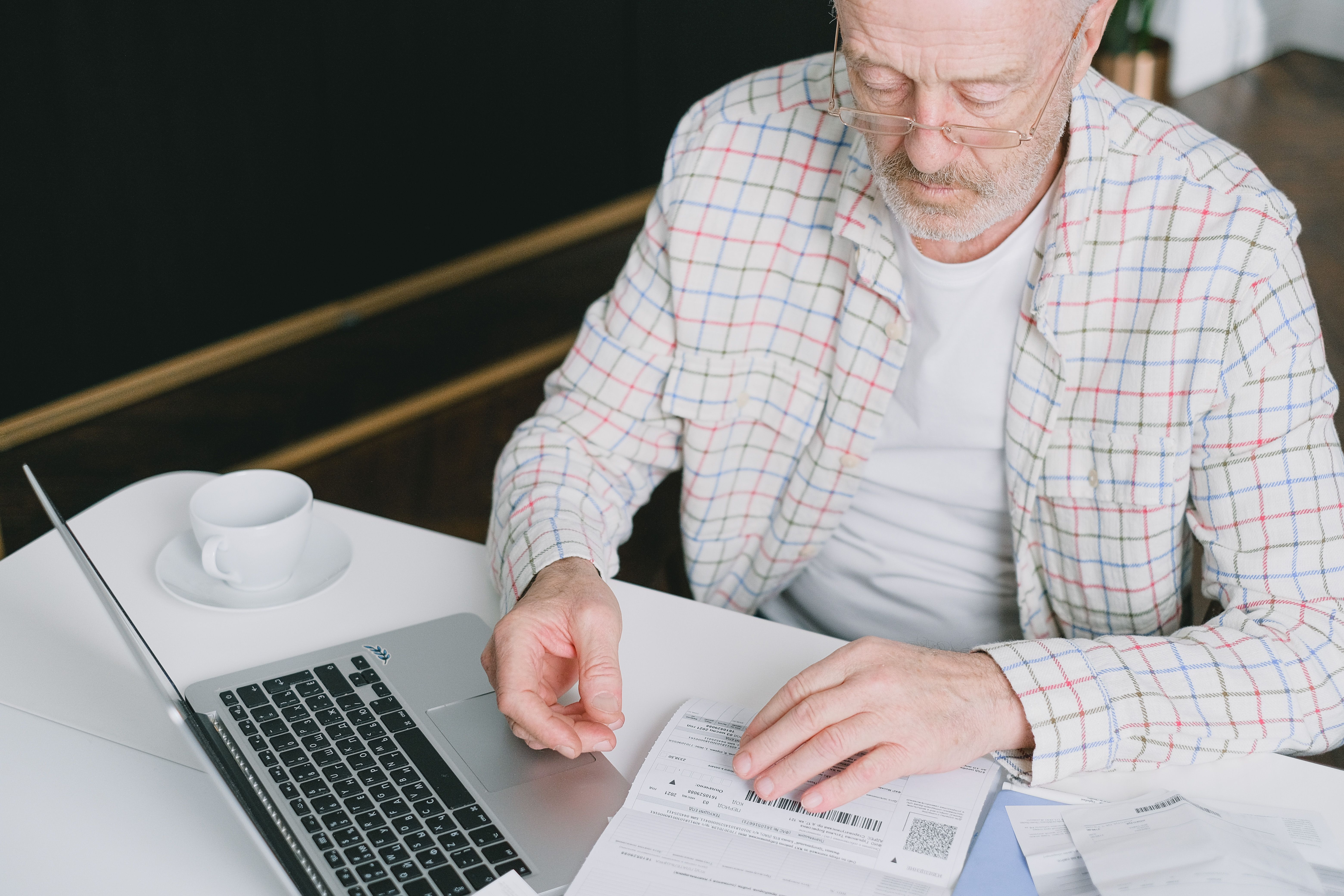 Un senior examine ses documents et relevés devant son ordinateur portable